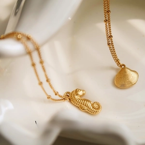 Macro detail of gold seahorse and shell pendants on beaded chains on a white tray