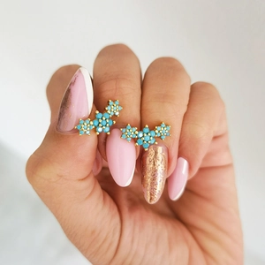 Macro shot of gold stud earrings featuring turquoise gemstone floral clusters on model