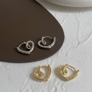 Close-up of heart-shaped twisted hoop earrings in gold and silver on leather background