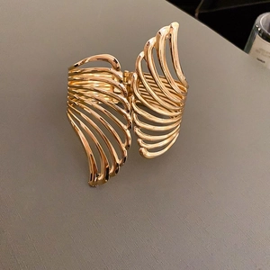 Macro detail of gold metal hollowed wing open cuff bracelet on smooth grey surface