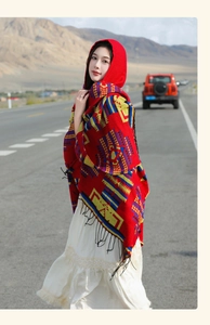 Ethnic red shawl with yellow geometric patterns and long tassels worn on scenic mountain road