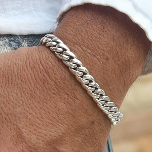 Macro view of polished silver Cuban link bracelet on wrist showing flat metal rings