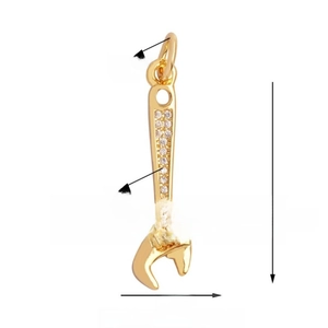 Macro detail of a gold wrench pendant encrusted with white crystals, size 25mm x 7mm