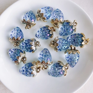 Detailed view of blue resin strawberry charms with pearl accents on a white tray