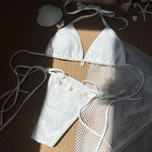 Flat lay of white crochet bikini with seashell details on a woven straw mat beach setting