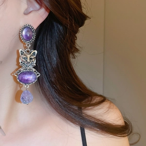 Detailed macro view of vintage cat drop earrings with purple crystals on a model's ear