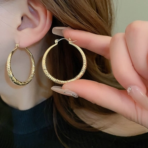 Close-up of gold hoop earrings with hammered texture being worn by a person