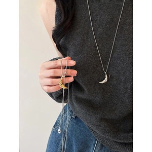 Gold and silver croissant pendant necklaces on long chains worn over a grey knit sweater