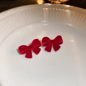 Élégantes boucles d'oreilles nœud en velours rouge sur un plat en céramique blanc