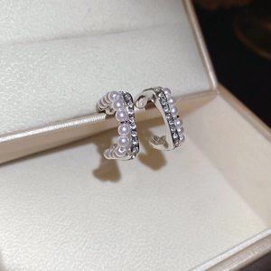 Macro detail of silver C-shaped hoop earrings with pearls and pavé cubic zirconia