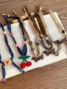 Flat lay of knit necklaces with crochet cherries and dachshund charms on a vintage book