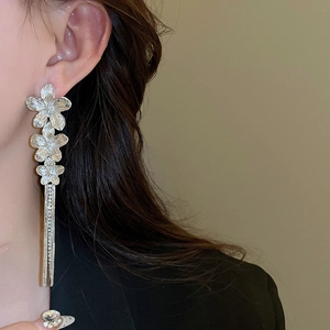 Elegant silver flower drop earrings with long metallic tassels worn by a model