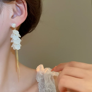 Detail of floral pearl tassel earrings featuring white layered petals and gold chains