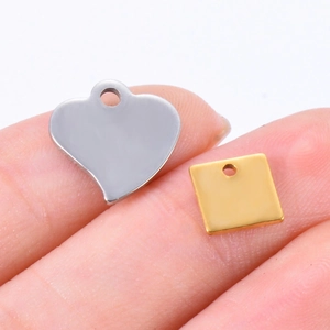 Close-up of tiny gold and silver heart and square stainless steel DIY charms on a fingertip