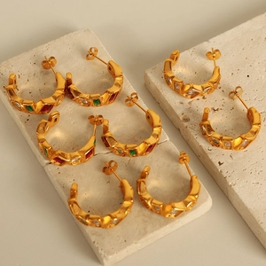 Golden C-shaped earrings with red, green, and clear gemstone inlays on textured stone