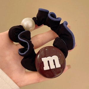Détail d'un chouchou en tissu avec perle et breloque en résine avec lettre M style chocolat