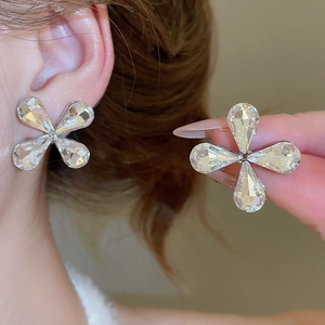 Detailed close-up of large clear crystal four-petal flower stud earrings on model