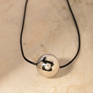 Detailed view of a polished silver sphere pendant on a black cord over a stone surface