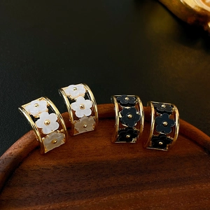 Detailed view of C-shaped floral earrings in gold with black and white resin petals