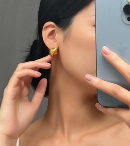 Dettaglio macro di orecchini a cerchio intrecciati placcati oro indossati da modella