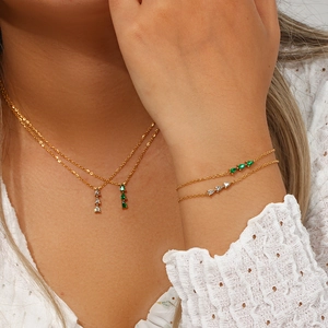 Detail of 18K gold-plated layered necklace and bracelet set with green pear-shaped gemstones