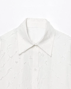 Détail du col de chemise blanc avec tissu à franges et bouton en résine