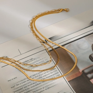 Detail of layered gold snake and paperclip chain necklace on a newspaper background