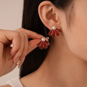 Close-up of a red fan-shaped earring with golden edges and a pearl on a model
