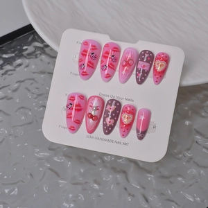 Detail of almond press-on nails with red lip designs, cherry charms, and bow accents