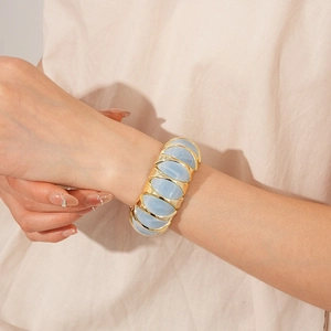 Detail of wide stretch bracelet featuring golden metal frames and light blue resin inserts