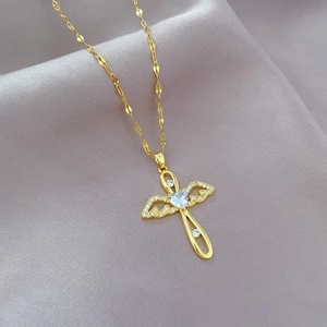 Detail of gold angel cross necklace with white zircon on silk fabric background