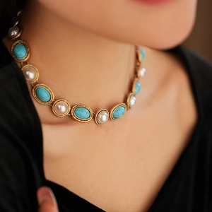 Close-up of vintage gold necklace with oval turquoise and round pearls on model