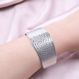 Detail shot of a silver wide cuff bracelet with a unique hammered pebble texture surface