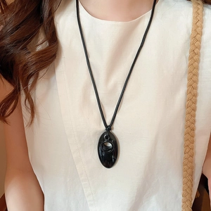 Close-up of a glossy black oval pendant necklace on a minimalist model wearing linen