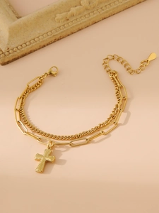 Détail du bracelet double couche doré avec pendentif croix et breloque en forme de cœur