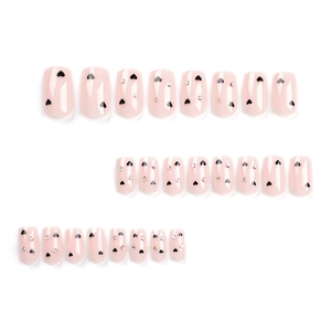 Pink press-on nails with black heart patterns and colorful rhinestones on white background