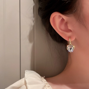 Close-up of golden heart earrings with rhinestones and white gemstone on a model