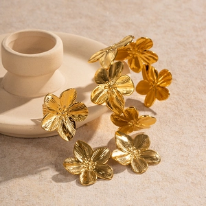 Golden flower jewelry set with brushed metal texture on beige ceramic and sand