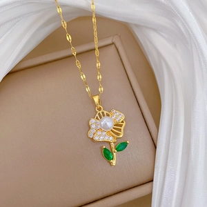 Detail of a gold flower necklace featuring a central pearl and green gemstone petals