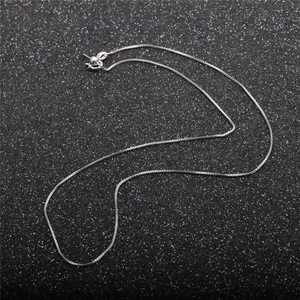 Detailed view of silver box chain necklace with ball clasp on a black glitter background