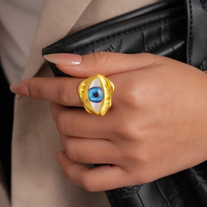 Close-up of chunky gold evil eye resin ring on hand over black quilted leather bag