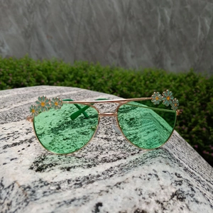 Close-up of kids daisy sunglasses with green lenses and gold frame on a stone