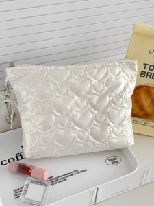 Detail of white quilted cosmetic bag with heart pattern and pearl charm on tray