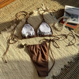 Detail view of brown bikini with beaded straps and shell charms on straw mat