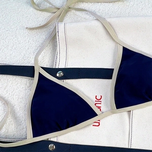 Detailed macro view of dark blue bikini top with beige piping and metal adjusters