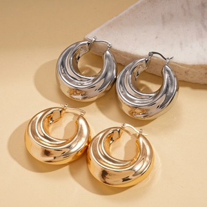 Polished gold and silver chunky round hoop earrings on a textured stone background