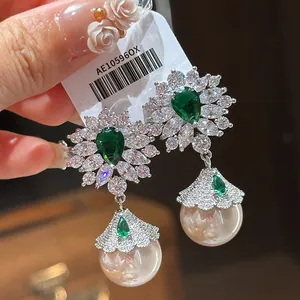 Detail of elegant silver drop earrings featuring green zircons and a white pearl bead