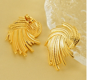 Detail of gold spiral earrings with woven texture and embossed dots on a neutral base