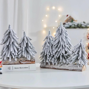 Mini snowy PE Christmas tree with wooden base on a cozy blurred home interior background