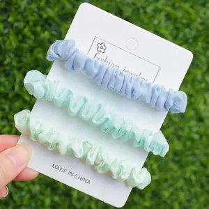 Lot de trois chouchous élastiques en tissu pastel sur carte blanche avec fond de jardin